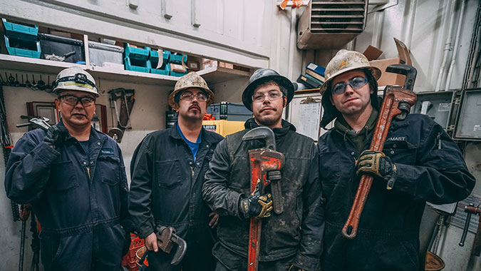 Four guys in hard hats working on a rig with large wrenches in their hands.